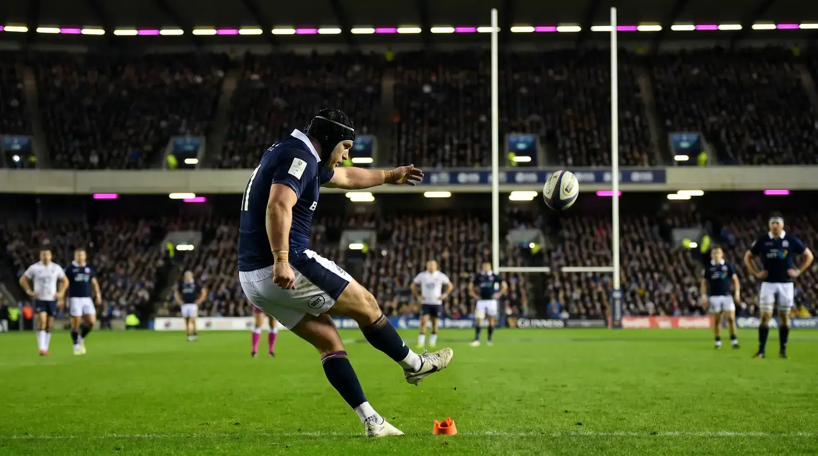 Rugby union fly-half kicking a conversion between the posts under floodlights